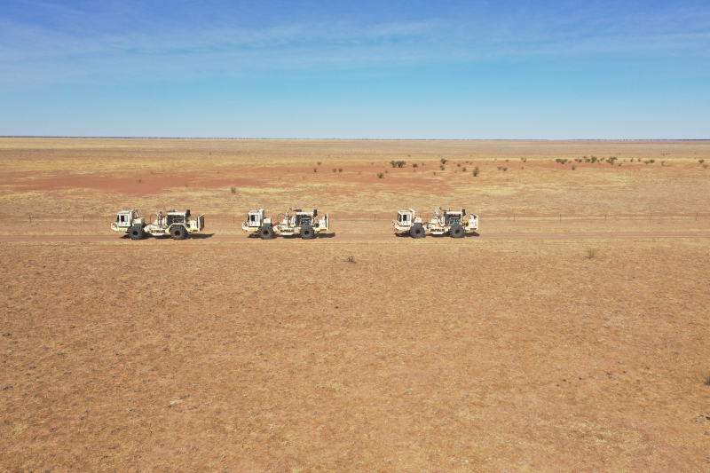 Wide view of a desert with three heavy vehicles driving across it