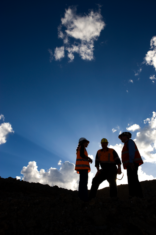 The silhouette of three people wearing high-visibility clothing, standing together talking